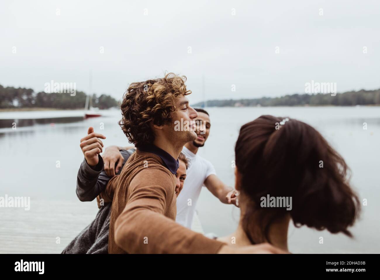 Lächelnde Freunde mit den Armen, die am Meer gegen den Himmel stehen Während der Ferien Stockfoto