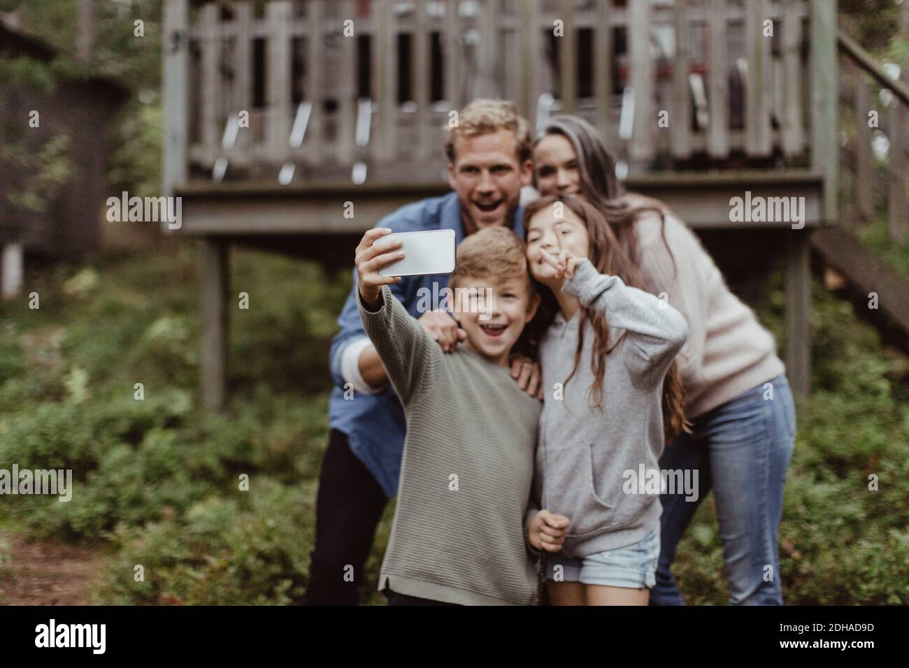 Lächelnde Familie, die Selfie mit dem Handy nimmt, während sie dagegen steht Haus Stockfoto