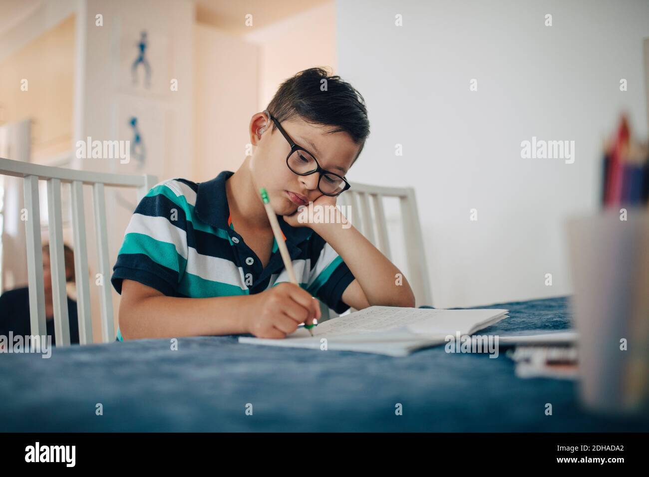 Nahaufnahme des behinderten Jungen, der auf Buch schreibt, während er an sitzt Tabelle Stockfoto