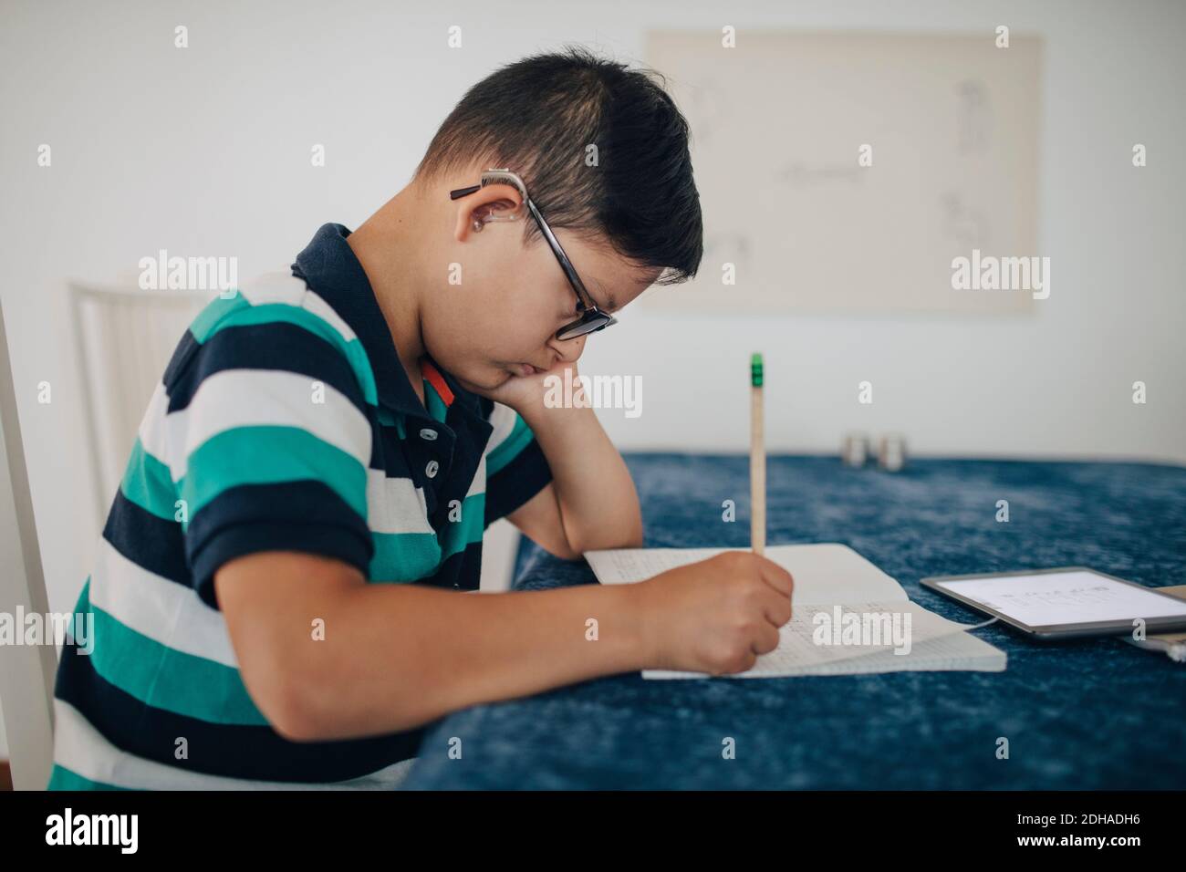 Seitenansicht eines behinderten Jungen, der im Sitzen auf einem Buch schrieb Am Tisch Stockfoto