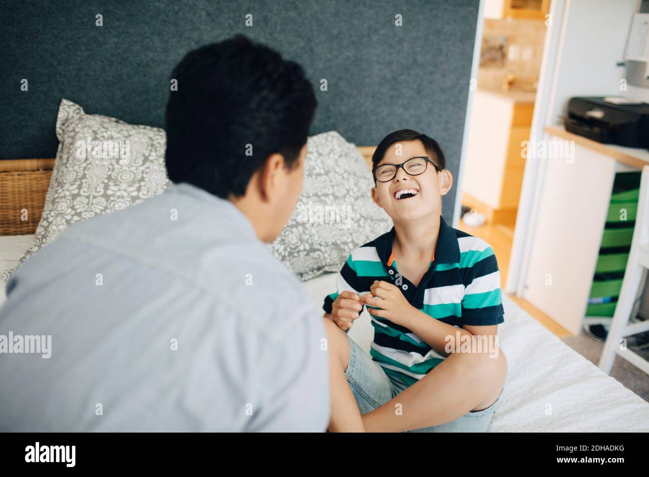 Lachender behinderter Junge, der zu Hause mit dem Vater auf dem Bett sitzt Stockfoto