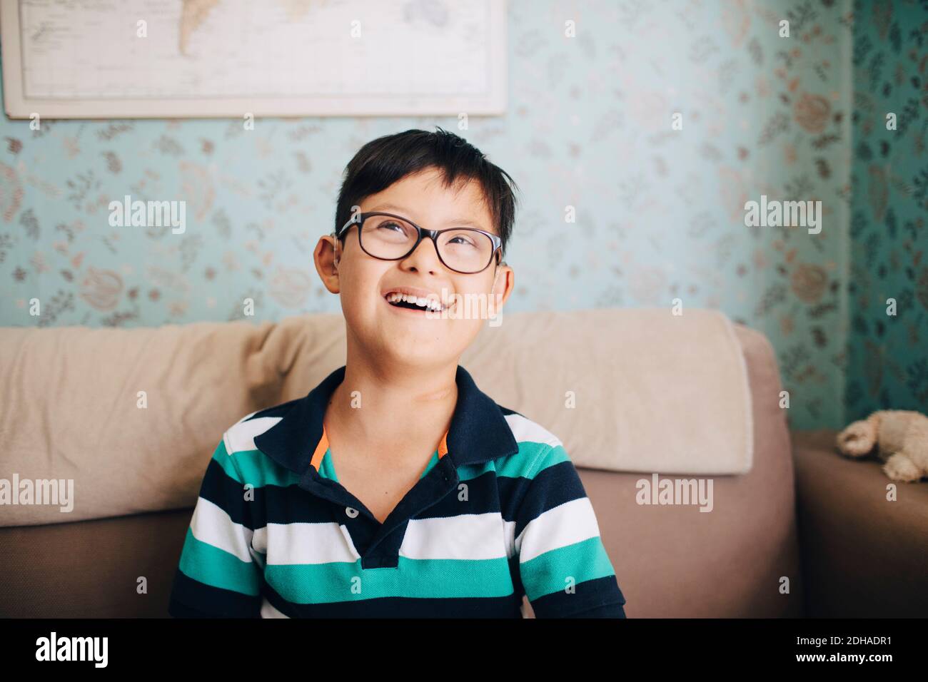 Nachdenklicher behinderter Junge lachend, während er zu Hause auf dem Sofa sitzt Stockfoto