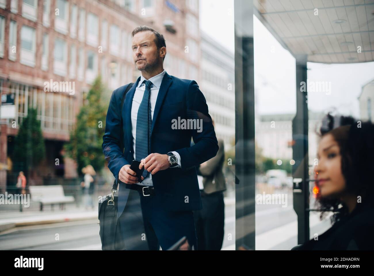 Geschäftsmann und Geschäftsfrau warten an der Bushaltestelle aus dem Glas gesehen Stockfoto