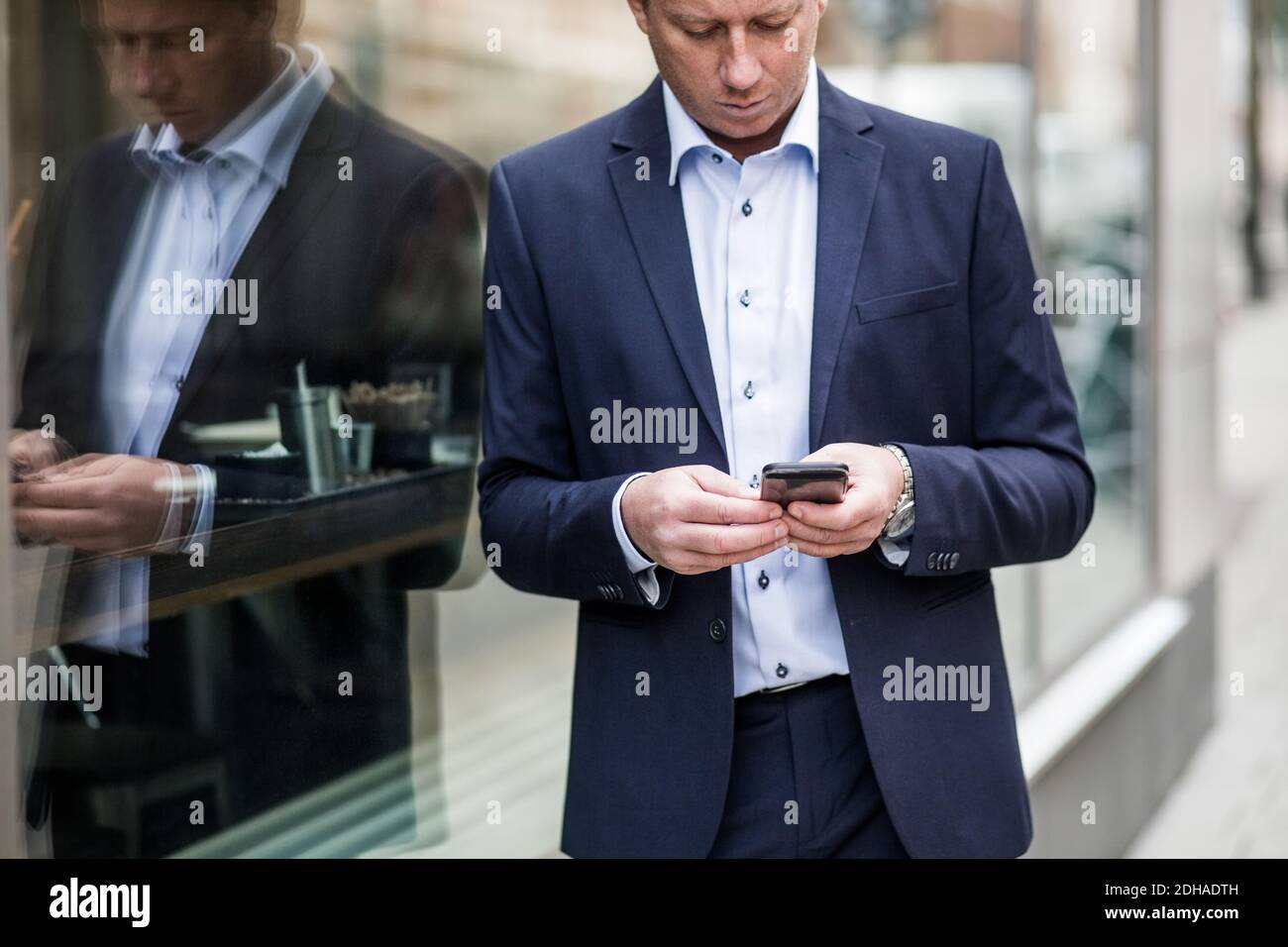 Erwägen reifen Geschäftsmann mit Smartphone, während Sie bei Glas stehen Angezeigt Stockfoto