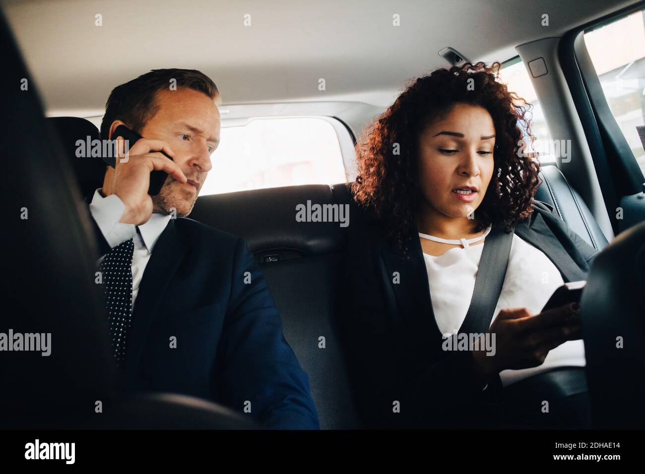 Geschäftsmann, der mit dem Mobiltelefon spricht, während er mit einer Kollegin sitzt Mit dem Taxi Stockfoto