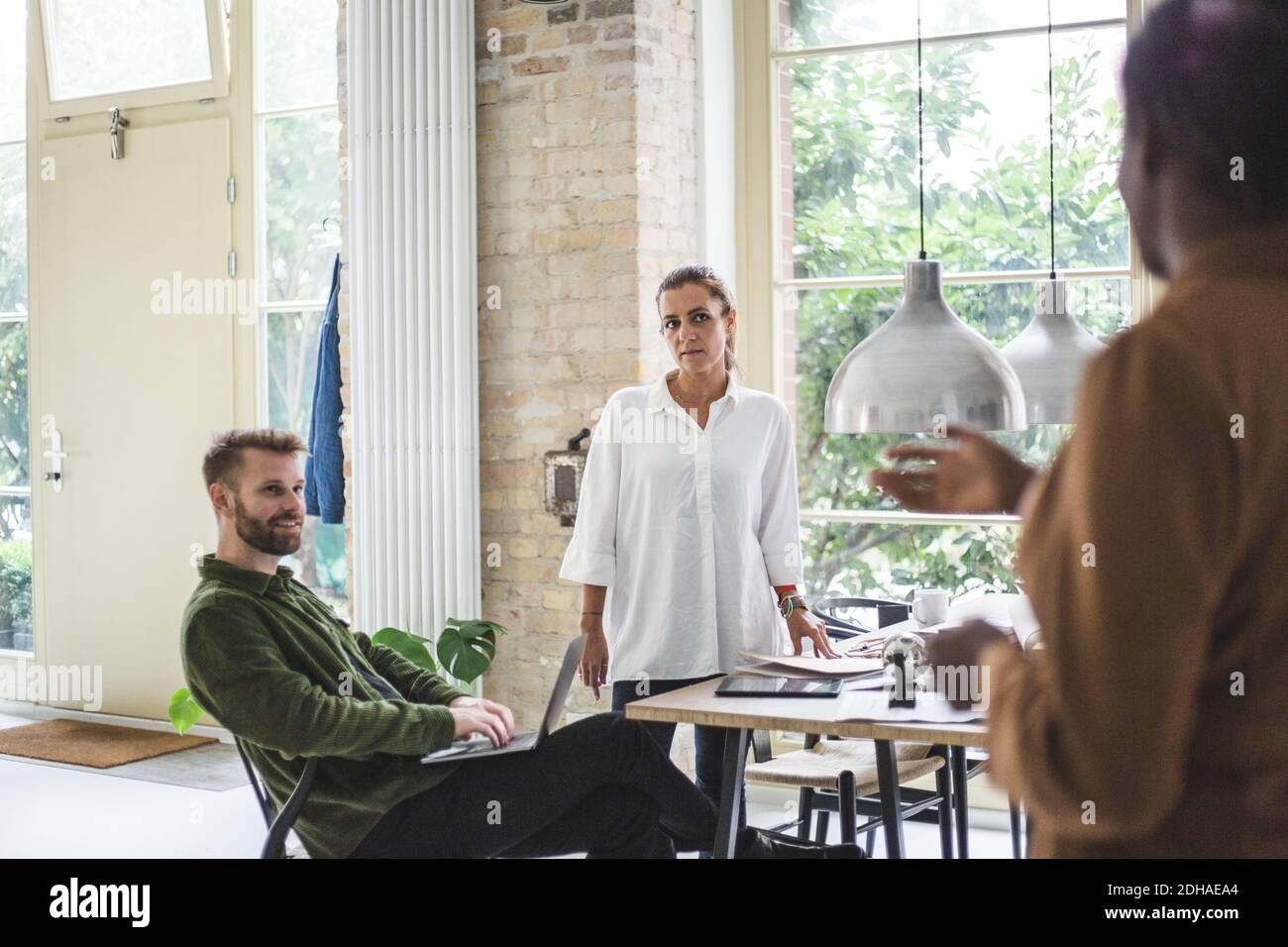 Mittlere Erwachsene Frau erklärt, während männliche und weibliche Unternehmer sitzen Im Home Office Stockfoto