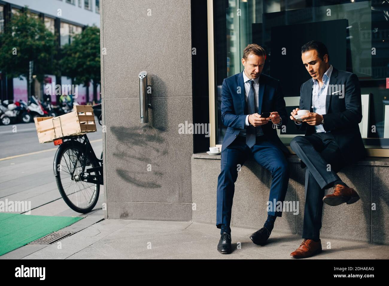 Reife männliche Geschäftskollegen sitzen mit Handy und Kaffee Tassen auf der Fensterbank im Café Stockfoto