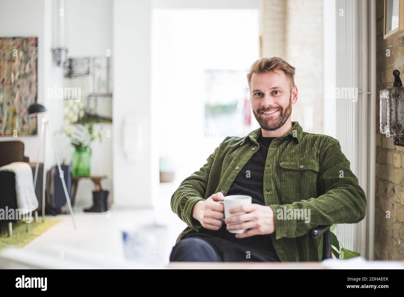 Porträt eines lächelnden männlichen Unternehmers mit Tasse zu Hause sitzen Büro Stockfoto