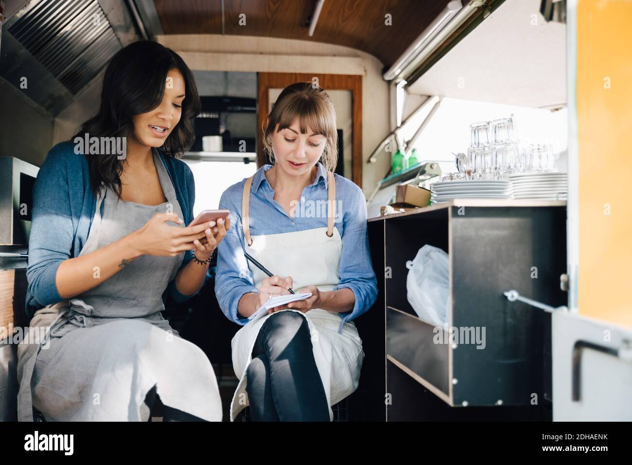 Weibliche Besitzerin, die Smartphone benutzt, während sie mit einem Kollegen sitzt Gewerbliches Landfahrzeug Stockfoto