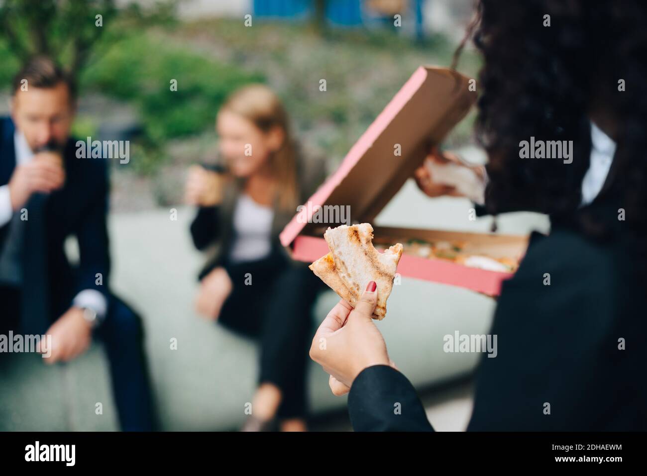 Beschnittenes Bild einer Geschäftsfrau, die Pizza gegen Kollegen hält Stockfoto