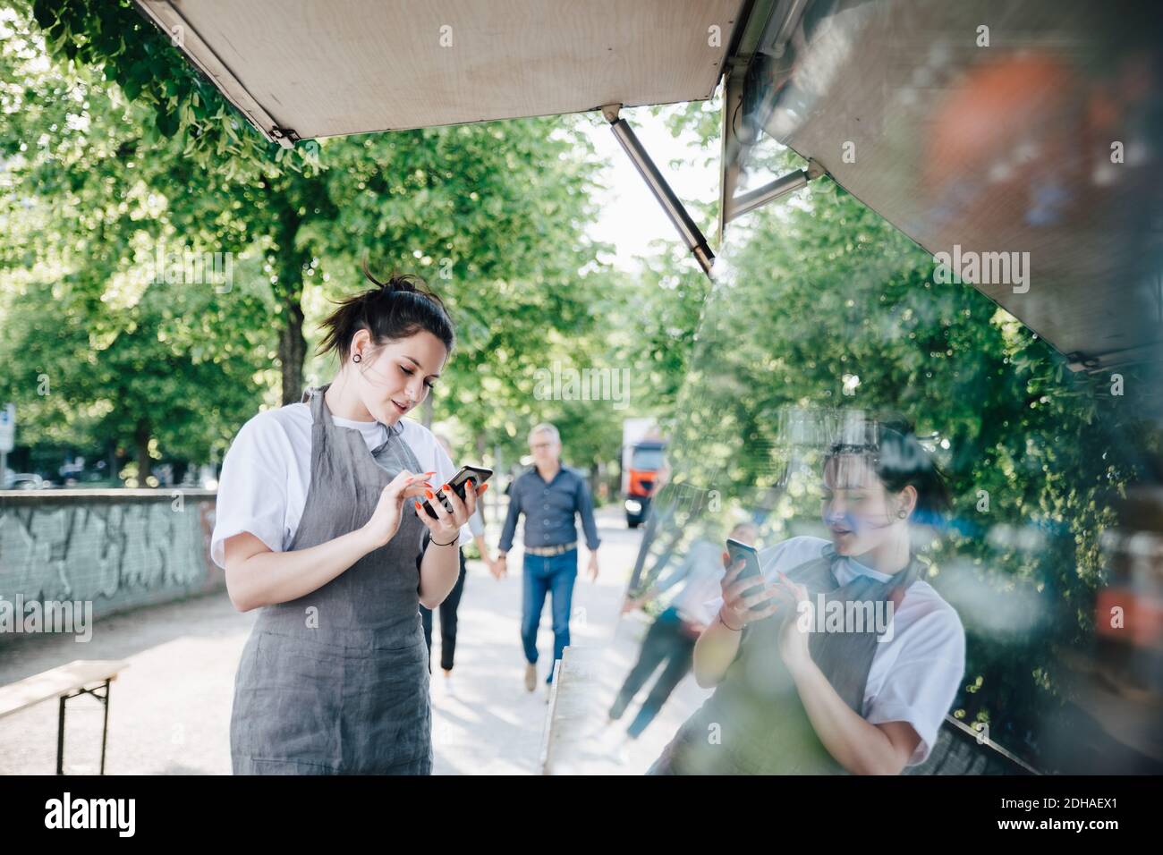 Weibliche junge Besitzerin, die Smartphone benutzt, während sie beim Essen steht LKW Stockfoto