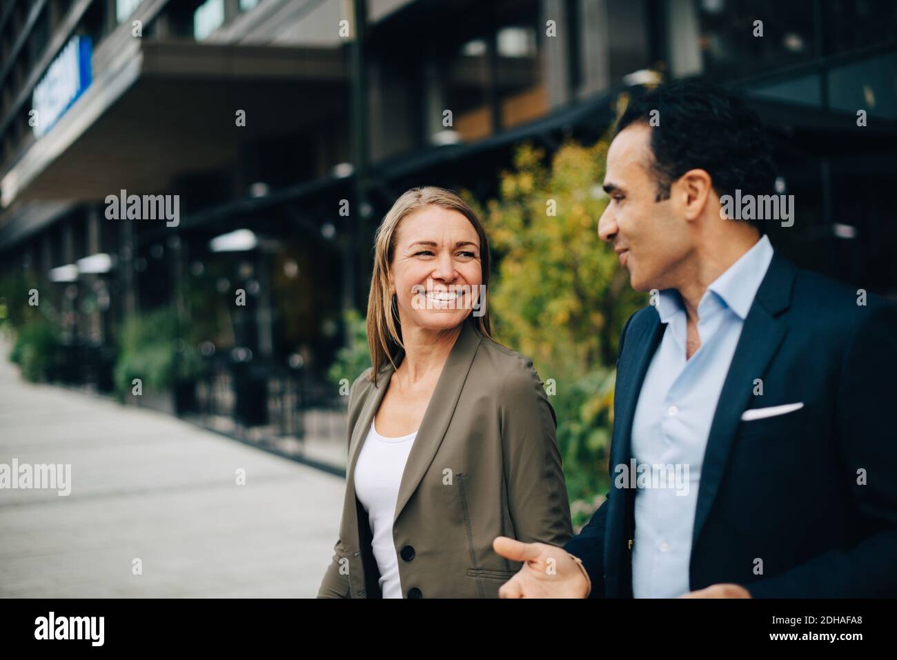 Lächelnde, reife Kollegen sprechen während sie in der Stadt spazieren Stockfoto