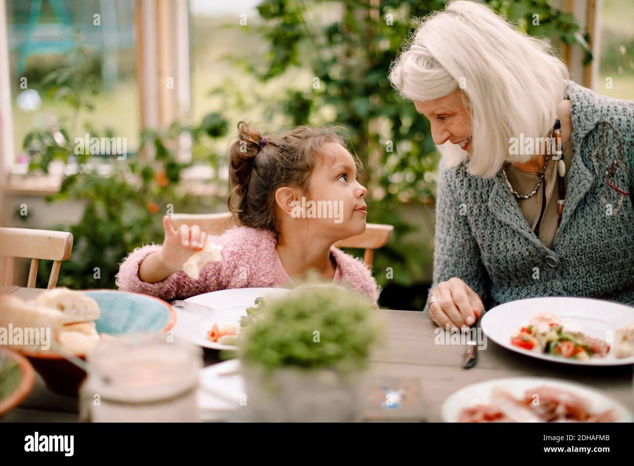 Lächelnde Großmutter, die Enkelin anschaut, während sie am Esstisch sitzt Während des Mittagessens Stockfoto