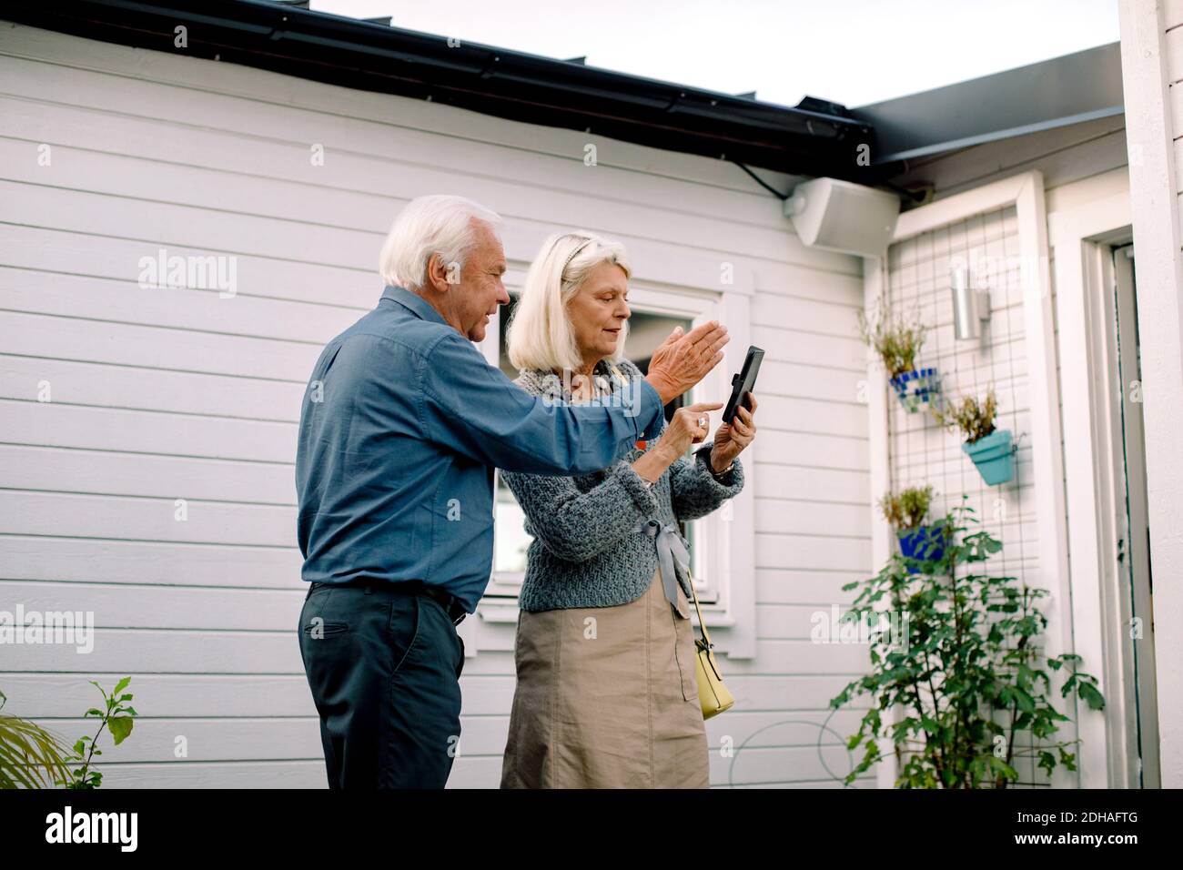 Älterer Mann im Gespräch mit einer Frau, die das Mobiltelefon gegen das Haus hält Stockfoto