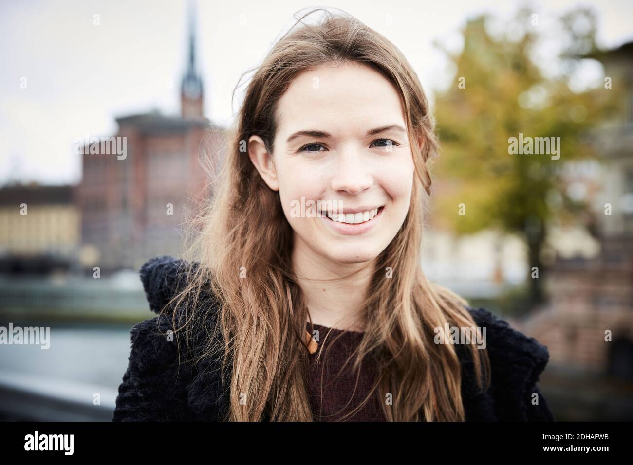 Nahaufnahme Porträt einer lächelnden jungen Frau mit braunen Haaren Stadt Stockfoto