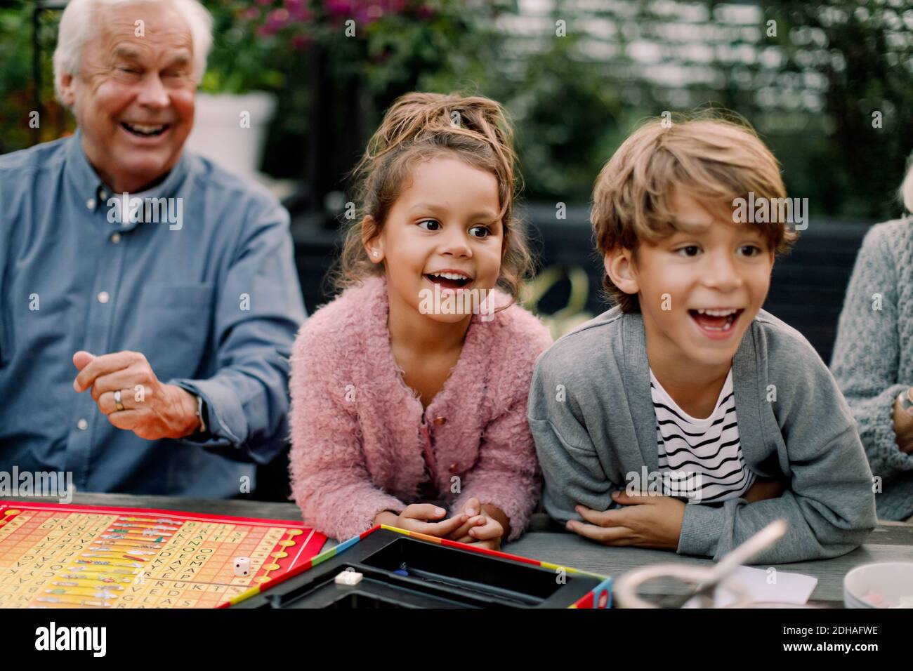 Lächelnde Enkelkinder spielen Brettspiel mit Großeltern auf dem Tisch in Hinterhof Stockfoto