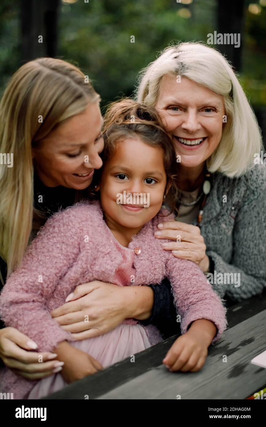 Porträt einer lächelnden Familie aus mehreren Generationen, die am Tisch im Hinterhof sitzt Stockfoto