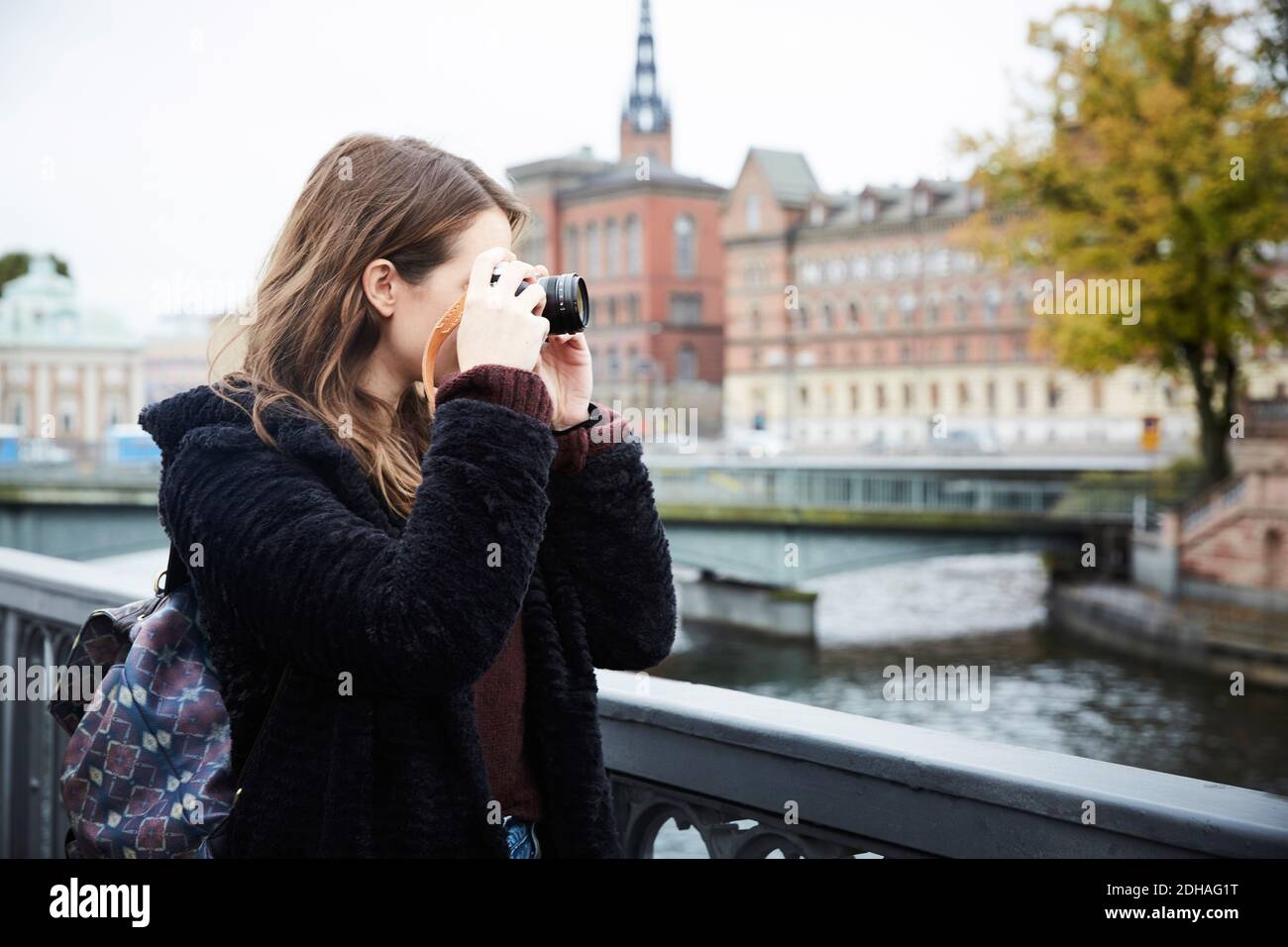 Junge Frau, die durch die Kamera fotografiert, während sie auf der Brücke steht Stadt Stockfoto