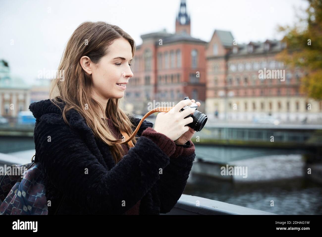 Lächelnde junge Frau mit Kamera auf Brücke in der Stadt stehen Stockfoto