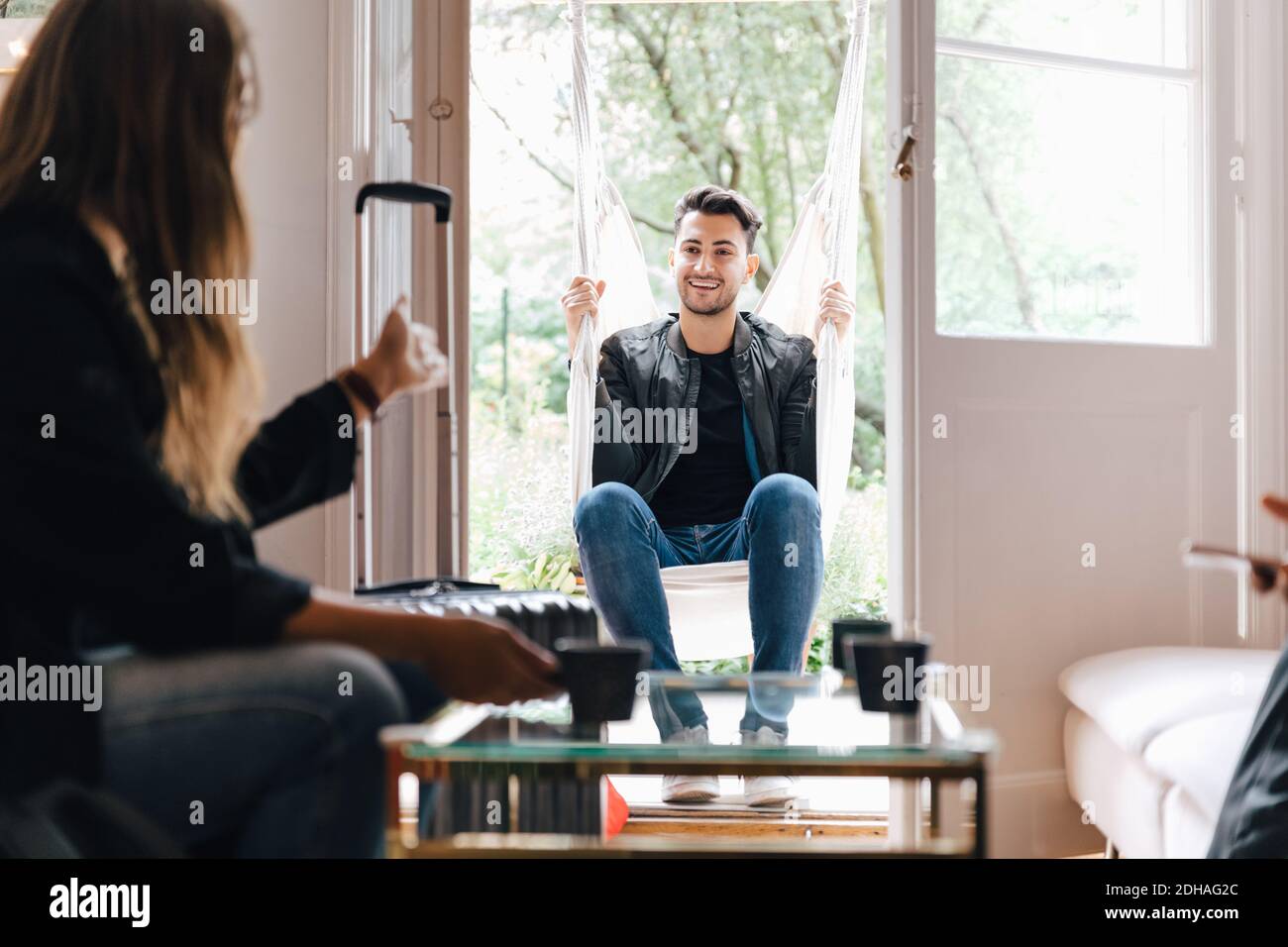 Junge Frau im Gespräch mit männlichen Freund sitzen in Schaukel an Wohnzimmer Stockfoto