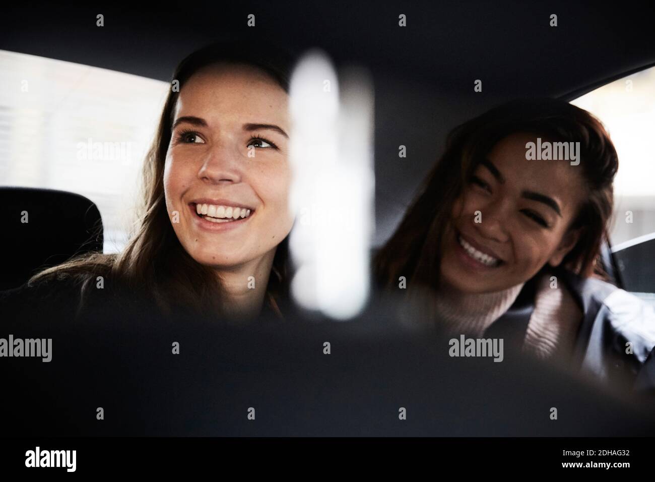 Lächelnde junge Freundinnen, die wegschauen, während sie im Taxi sitzen Stockfoto