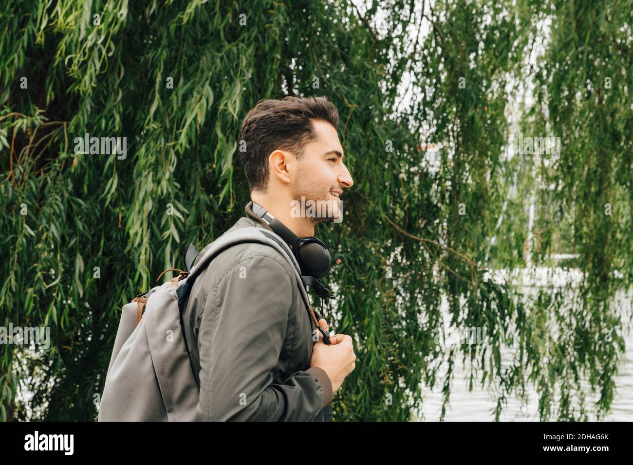 Seitenansicht des jungen Mannes mit Rucksack, der am Baum steht In der Stadt Stockfoto