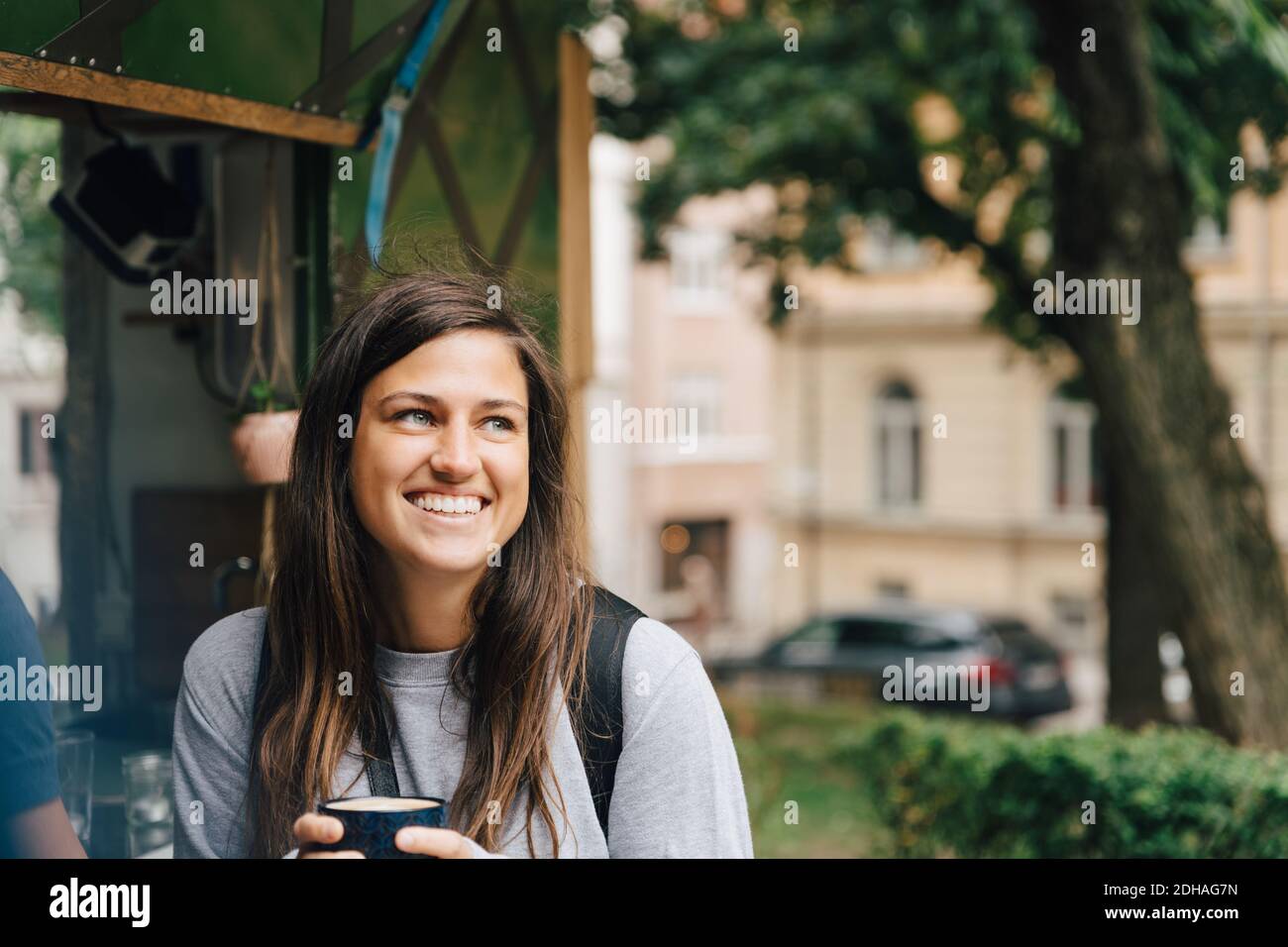 Lächelnde Frau hält Kaffeetasse, während sie am Konzessionsständer sitzt In der Stadt Stockfoto