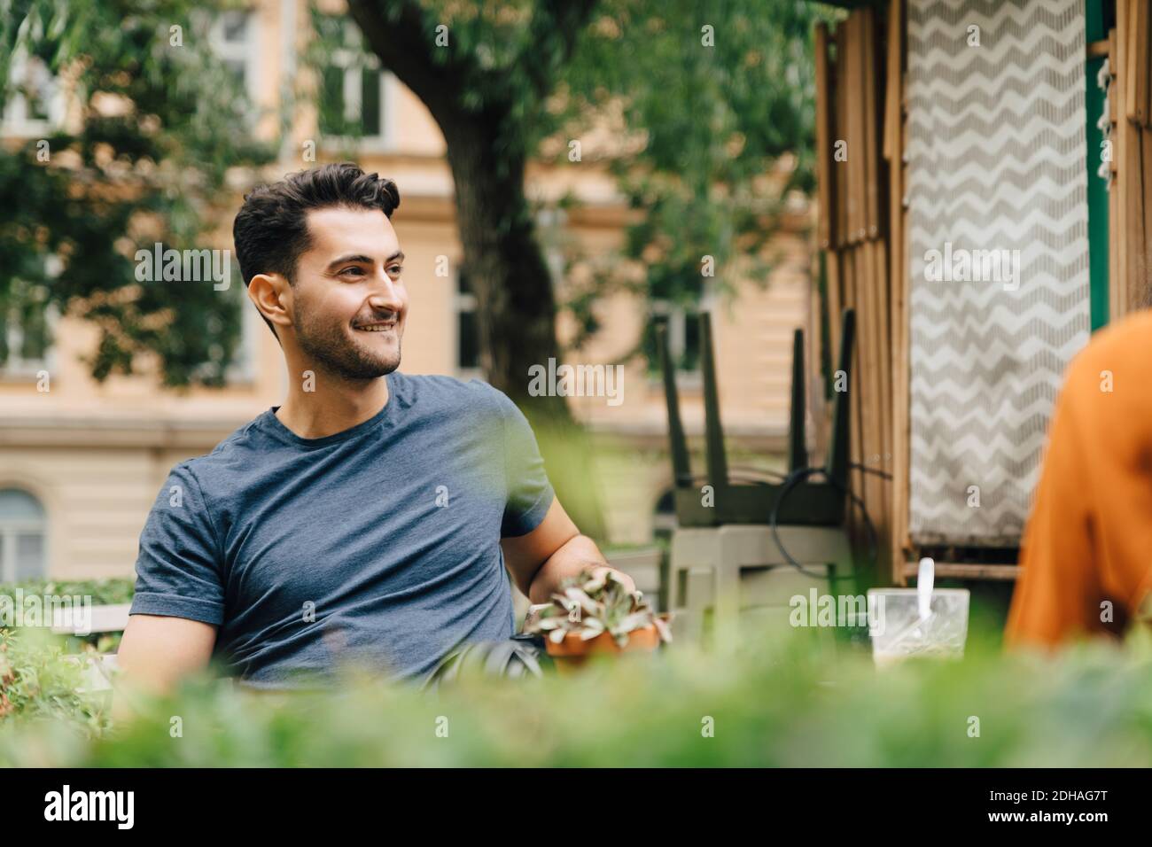 Lächelnder junger Mann, der mit einem Freund im Restaurant in der Stadt sitzt Stockfoto