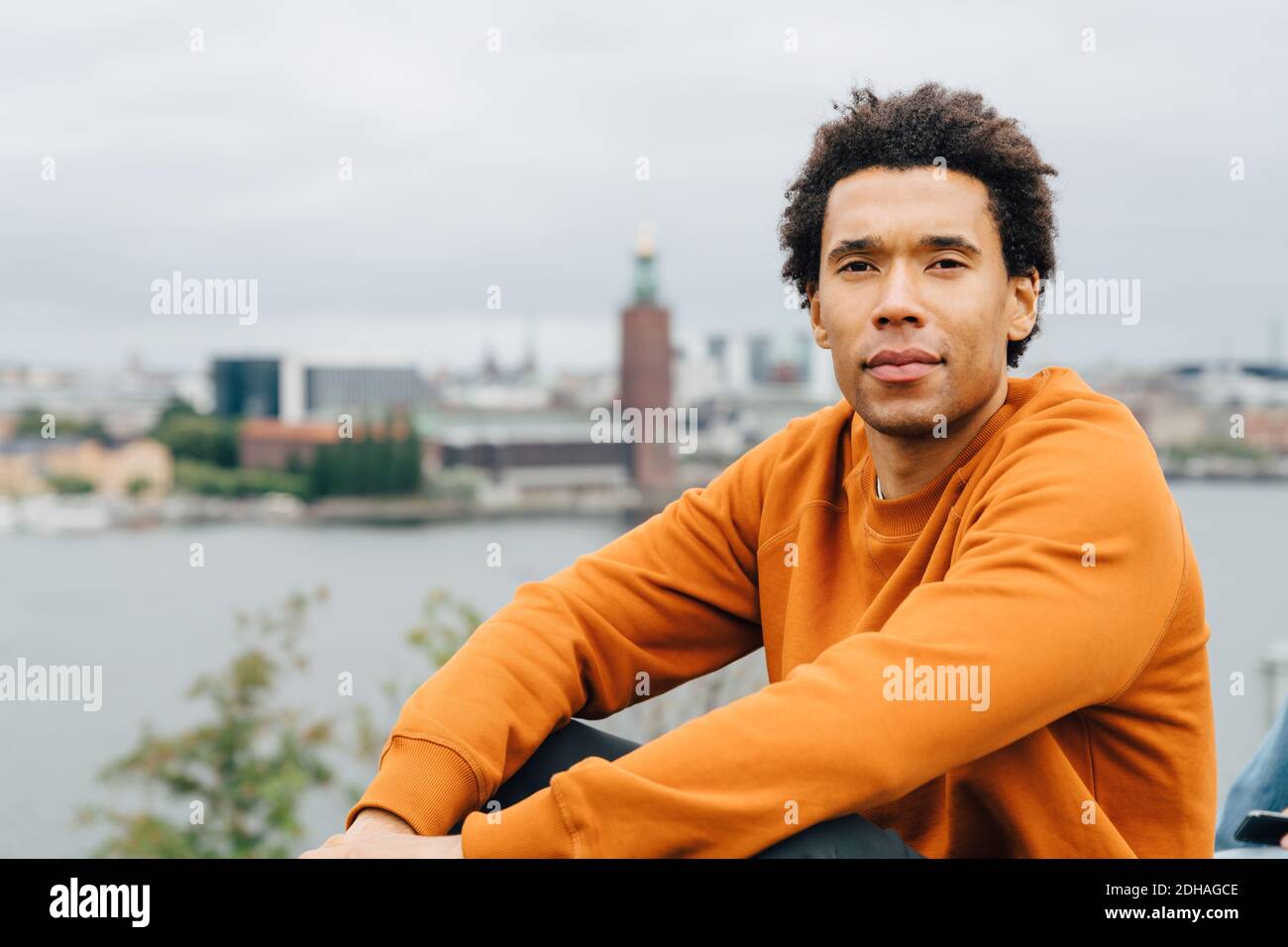 Porträt eines jungen Mannes, der am Stadtbild gegen den Himmel sitzt Stockfoto