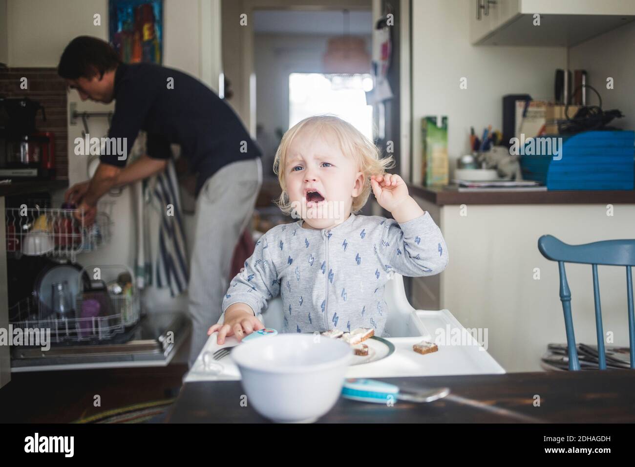 Weinendes männliches Kleinkind, das wegschaut, während es auf einem Hochstuhl sitzt In der Küche in der Wohnung Stockfoto