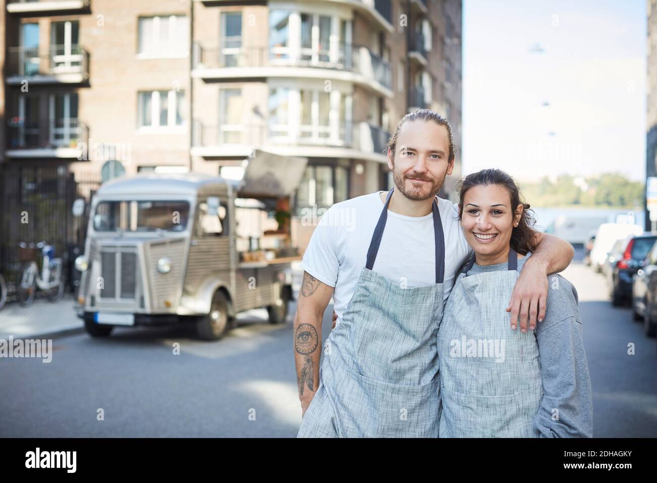 Porträt von selbstbewussten männlichen und weiblichen Besitzern, die Arme um sich herum stehen Mit Foodtruck im Hintergrund Stockfoto