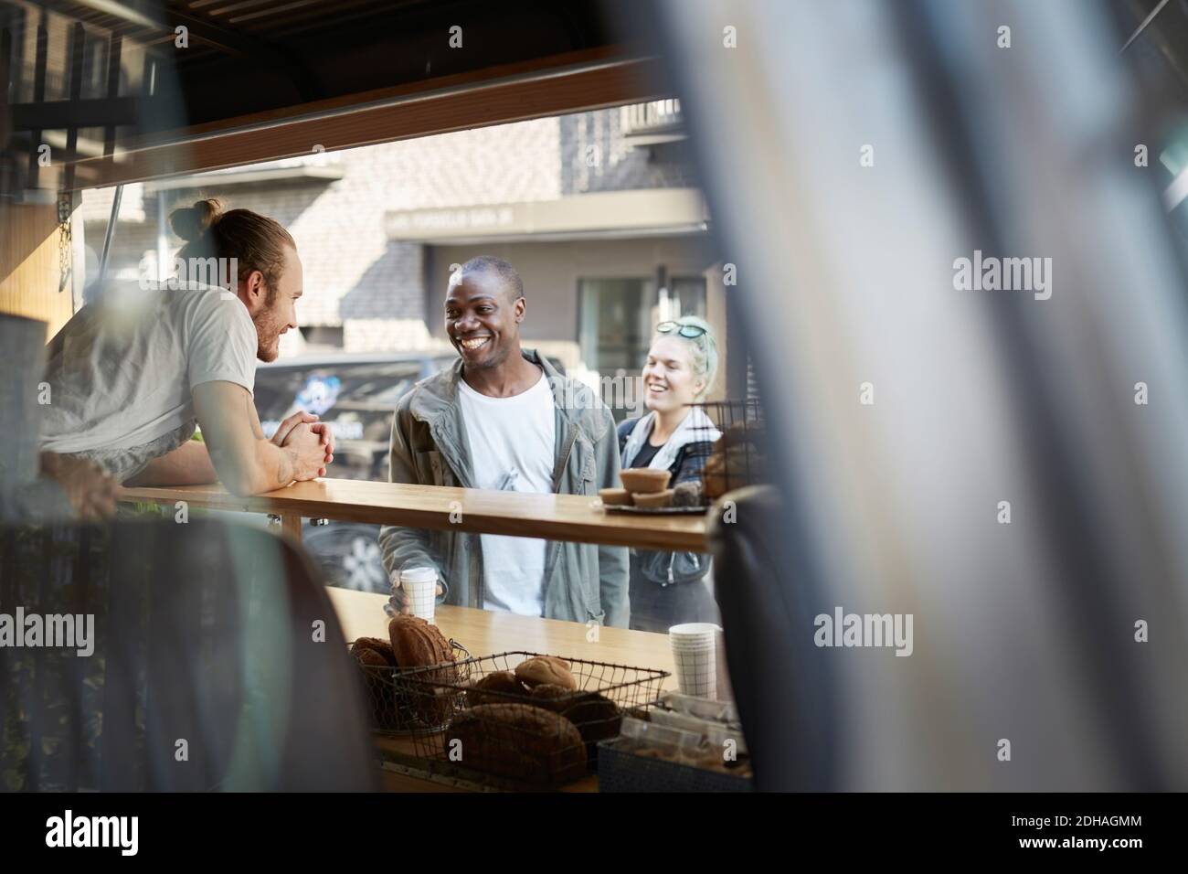 Lächelnder, mittelerwachsener Mann, der mit dem Verkäufer am Foodtruck spricht Stockfoto Lächelnder, mittelerwachsener Mann, der mit dem Verkäufer am Foodtruck spricht Stockfoto