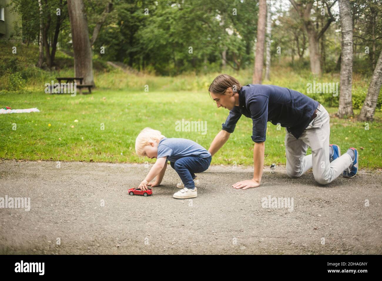 Vater kniet, während Sohn mit Spielzeugauto auf dem Fußweg spielt Gegen Pflanzen im Park Stockfoto
