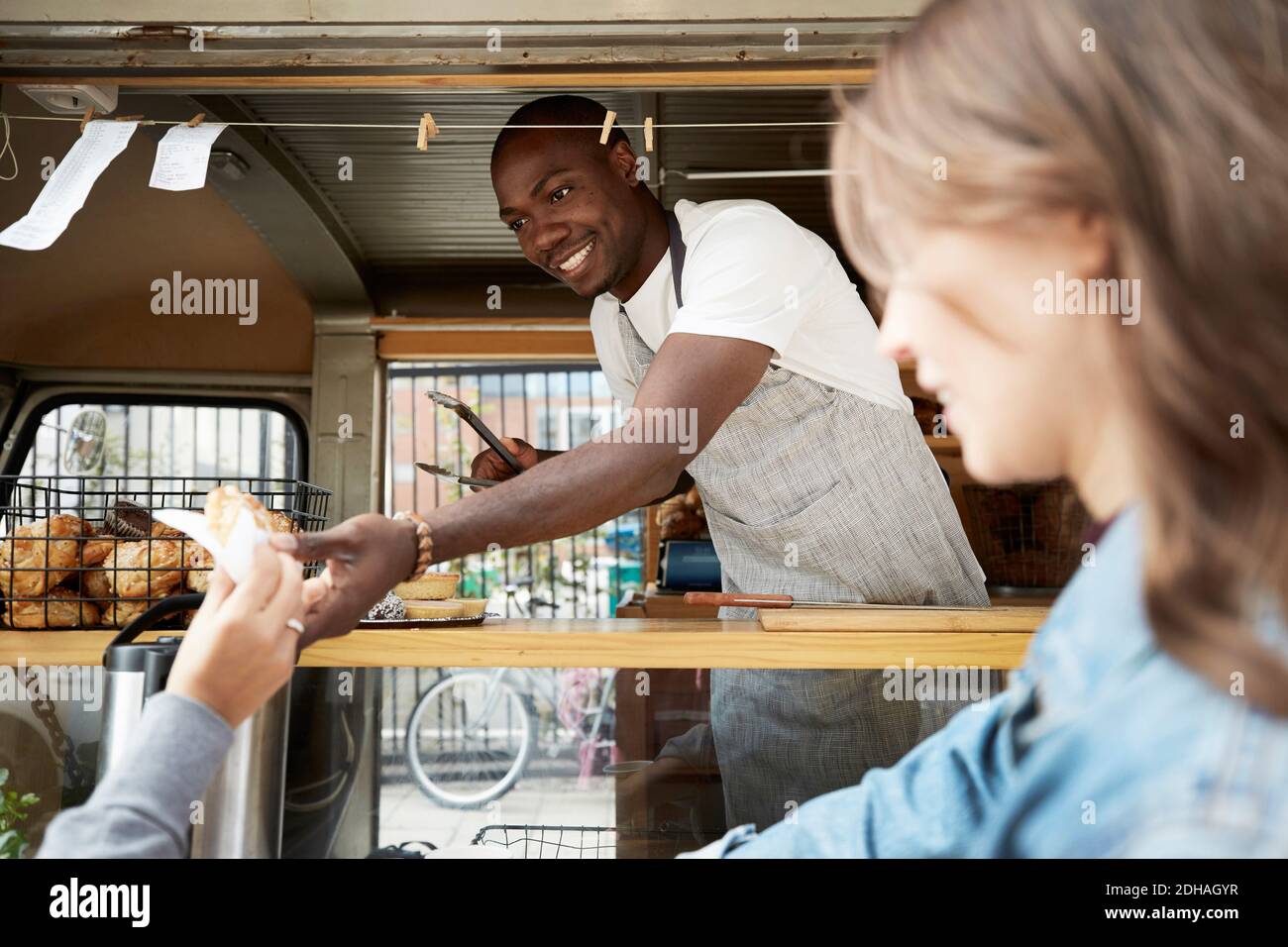 Verkäufer mit mittlerem Erwachsenenalter, der dem Kunden am Food Truck Brot überreicht Stockfoto