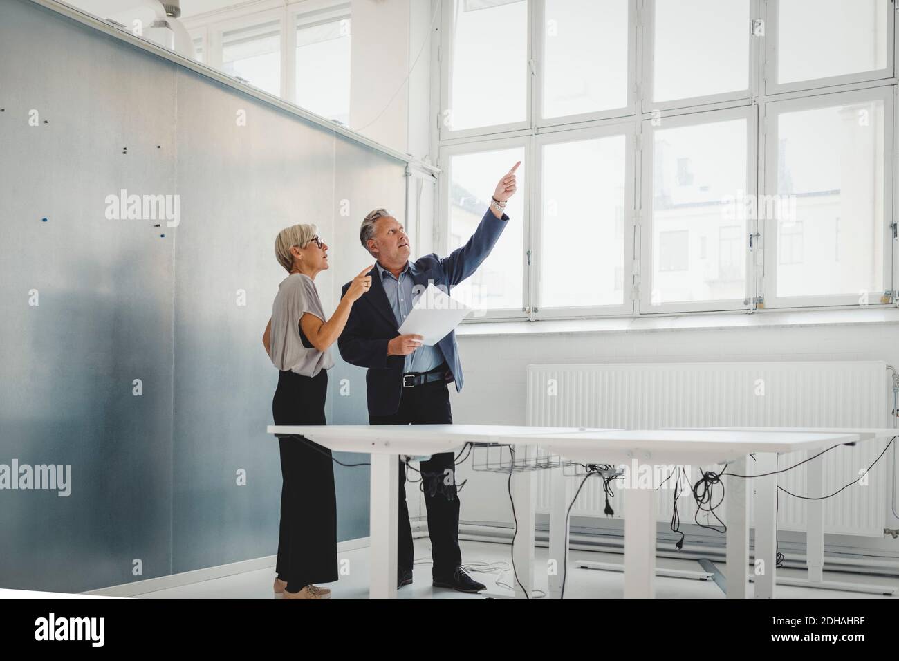 Volle Länge des Geschäftsmannes, der Dokumente hält, während er mit Frau diskutiert Kollege in neuem Büro Stockfoto