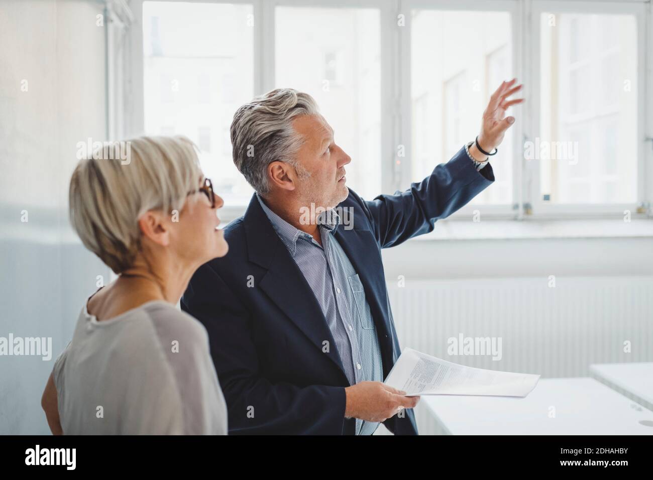 Reifer Geschäftsmann, der Dokumente hält, während er mit einer Kollegin spricht Neues Büro Stockfoto