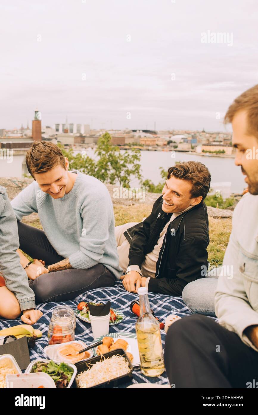 Glückliche männliche Freunde genießen Essen während Picknick gegen Himmel Stockfoto