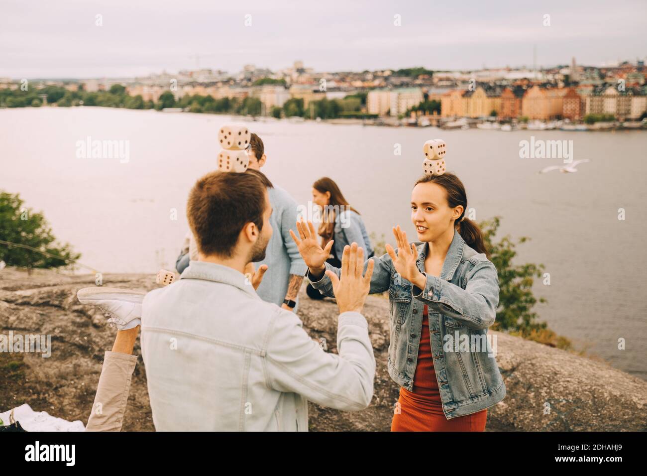 Männliche und weibliche Freunde spielen Balancierspiele, während sie auf stehen Feld am See Stockfoto