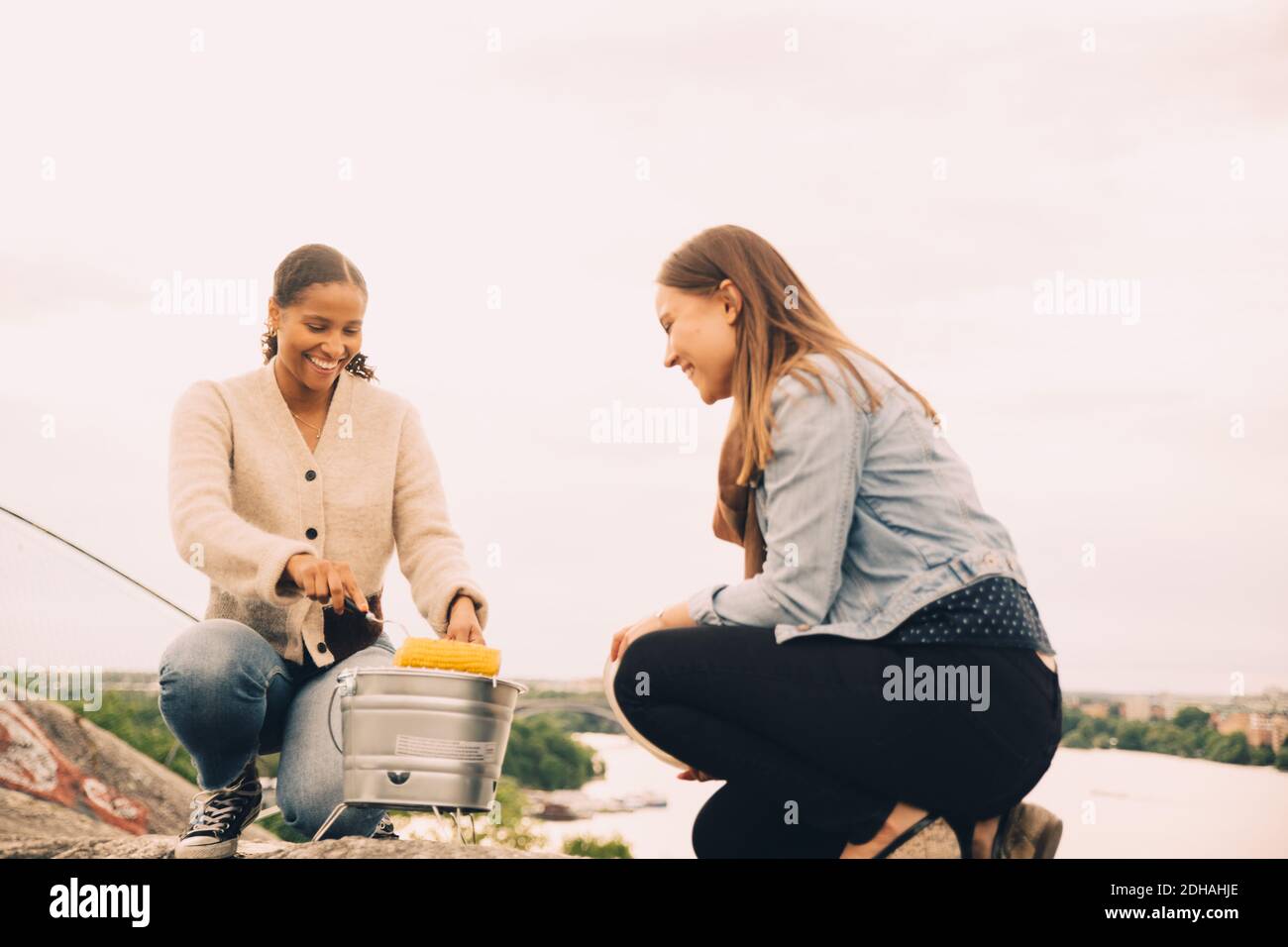 Lächelnde Freundinnen rösten im Picknick am Himmel die Süßkorne Stockfoto
