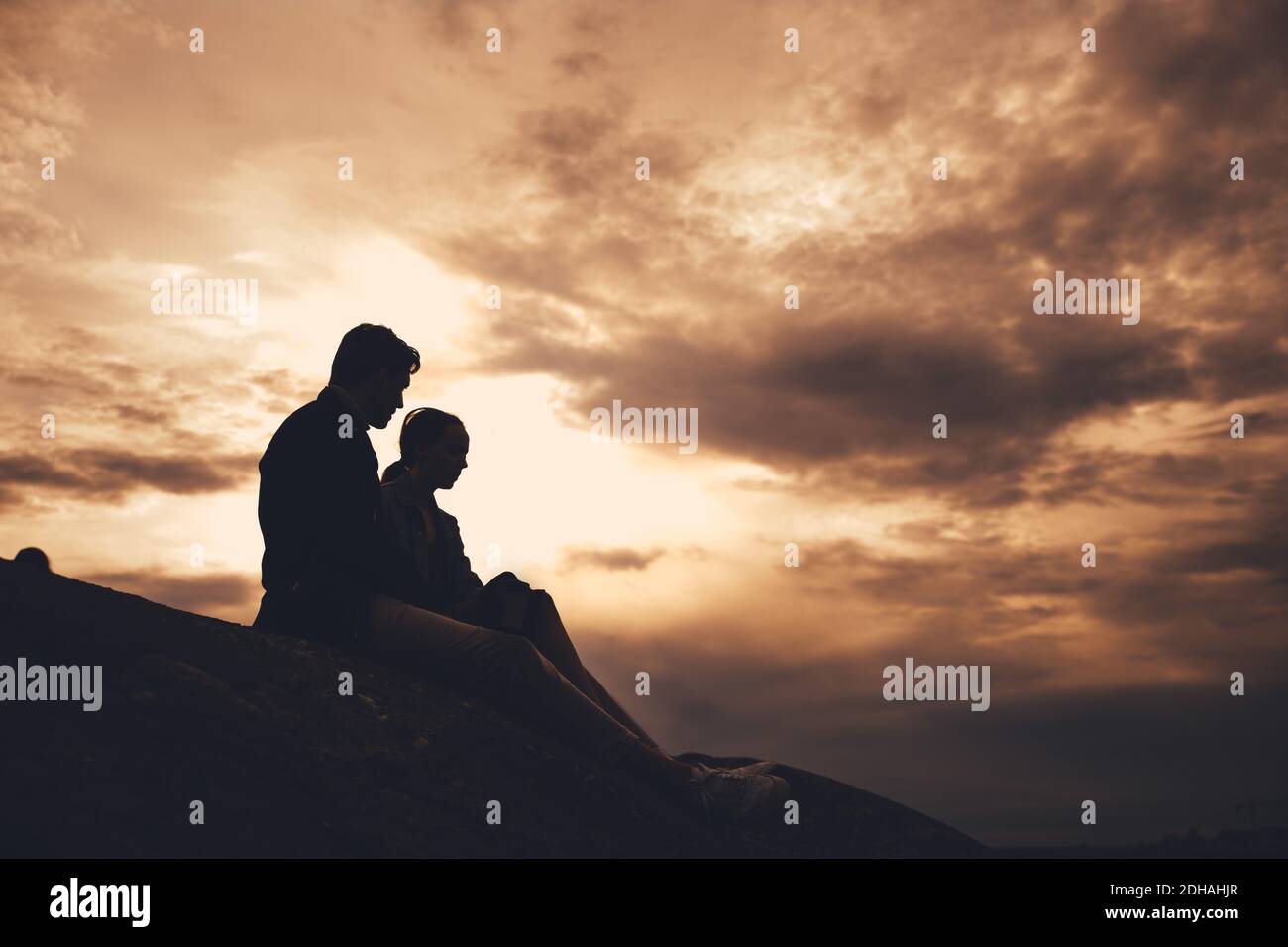 Low-Winkel-Ansicht der Silhouette Freunde sitzen auf Felsformation Es weht schwacher bewölktes Wetter Stockfoto