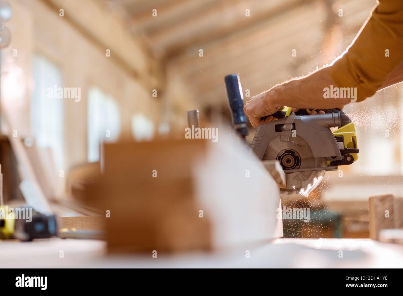 Zimmermann sägt Holzstäbe mit schnurloser elektrischer Säge in der Tischlerwerkstatt. Nahaufnahme ohne Gesicht Stockfoto
