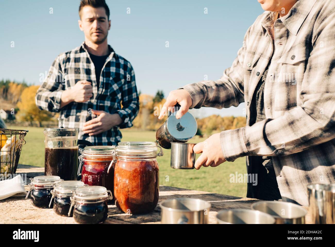 Mid adult männlich Landwirt Blick auf Frau Gießen Kaffee in cup auf dem Bauernmarkt Stockfoto