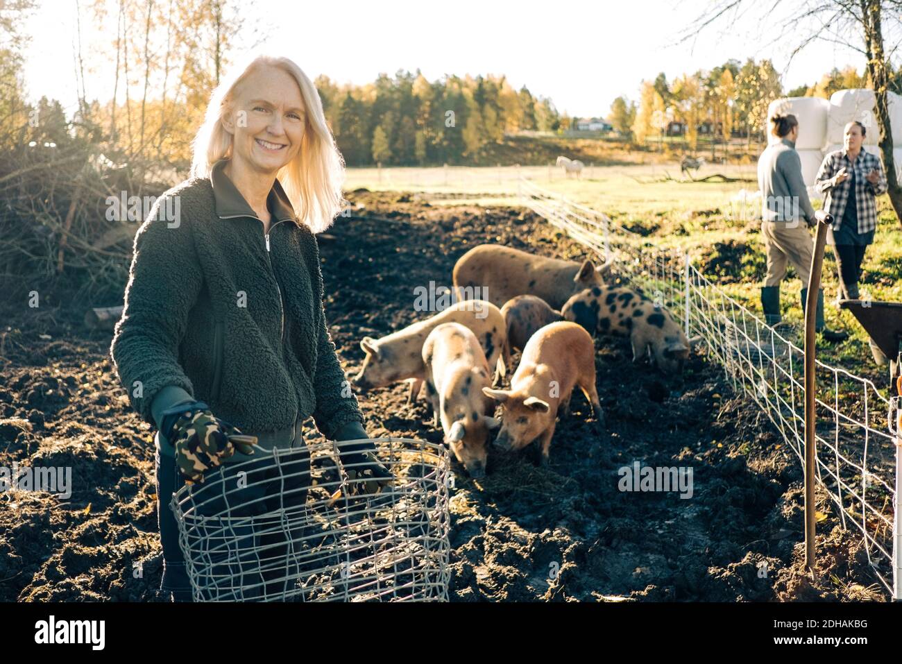 Portrait einer lächelnden Bäuerin, die einen leeren Korb mit Schweinen hält Beweidung auf Bio-Bauernhof Stockfoto