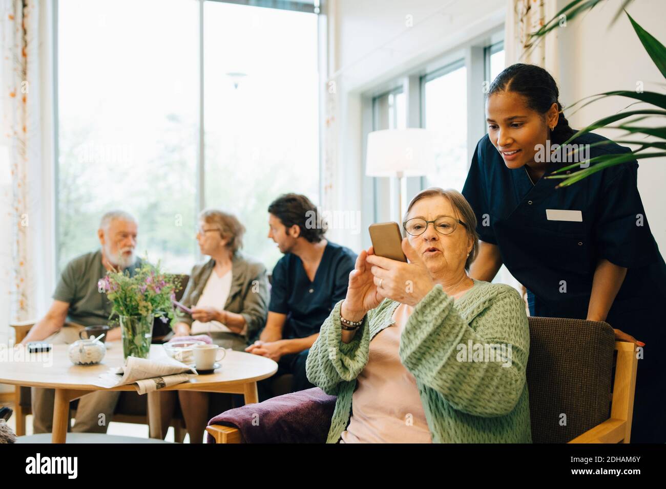 Ältere Frau im Ruhestand, die ein Smartphone mit einer jungen Krankenschwester teilt Bei der Öffentlichkeitsarbeit Stockfoto