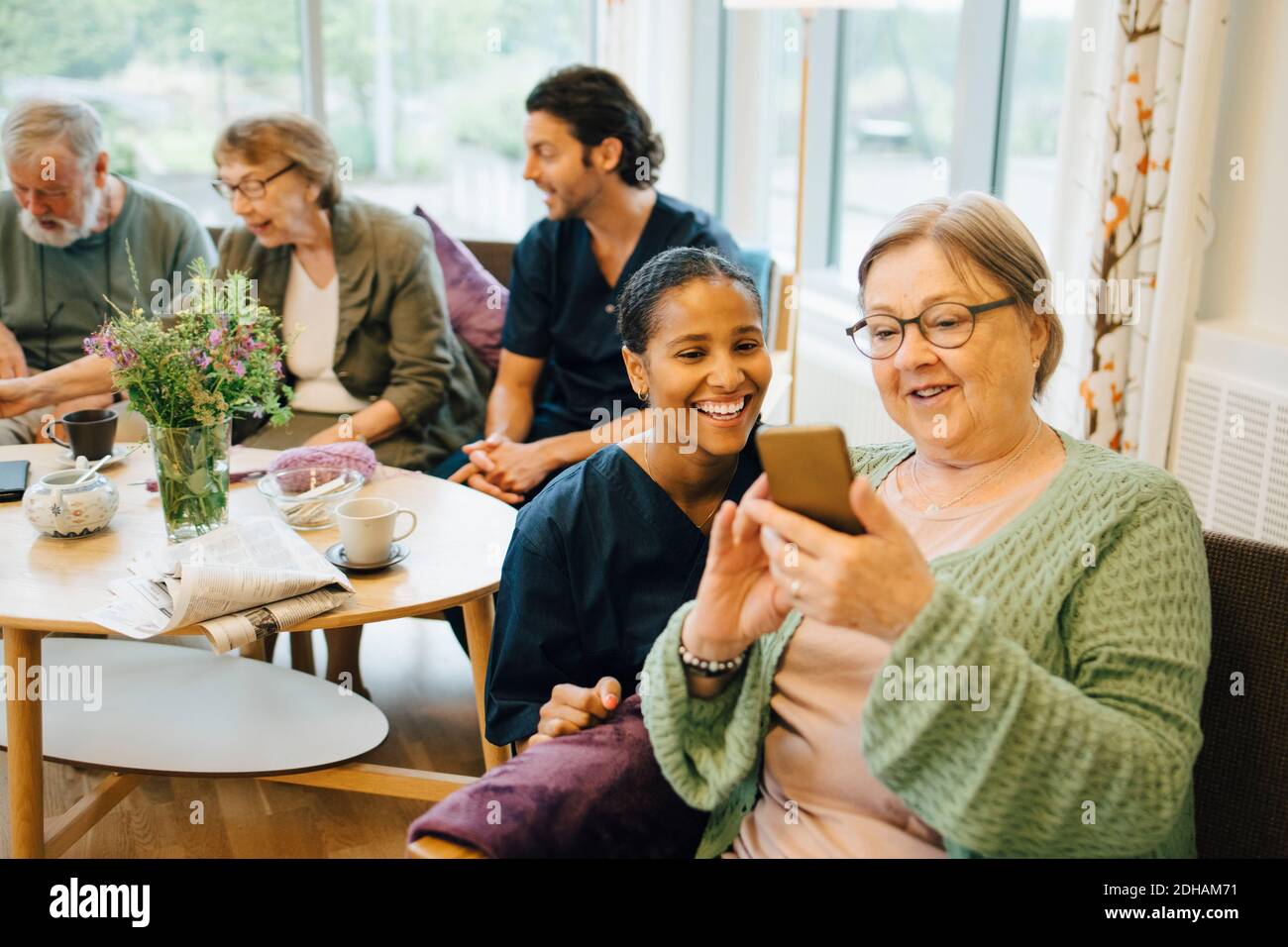 Ältere Frau im Ruhestand, die ein Smartphone mit einer lächelnden jungen Frau teilt Krankenschwester bei der Öffentlichkeitsarbeit Stockfoto