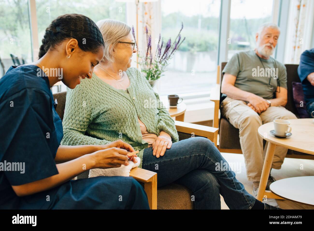 Junge weibliche Hausmeisterin Feilen Senior Frau Nagel während sitzen Pflegeheim Stockfoto