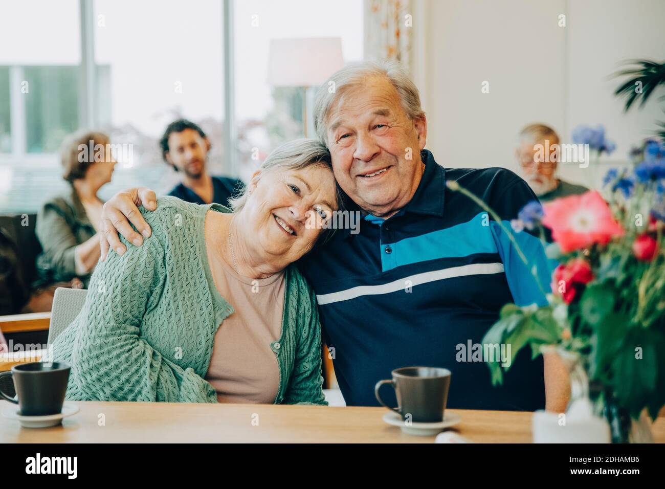 Porträt älterer älterer Freunde, die mit dem Arm um sich herum sitzen Esstisch im Pflegeheim Stockfoto