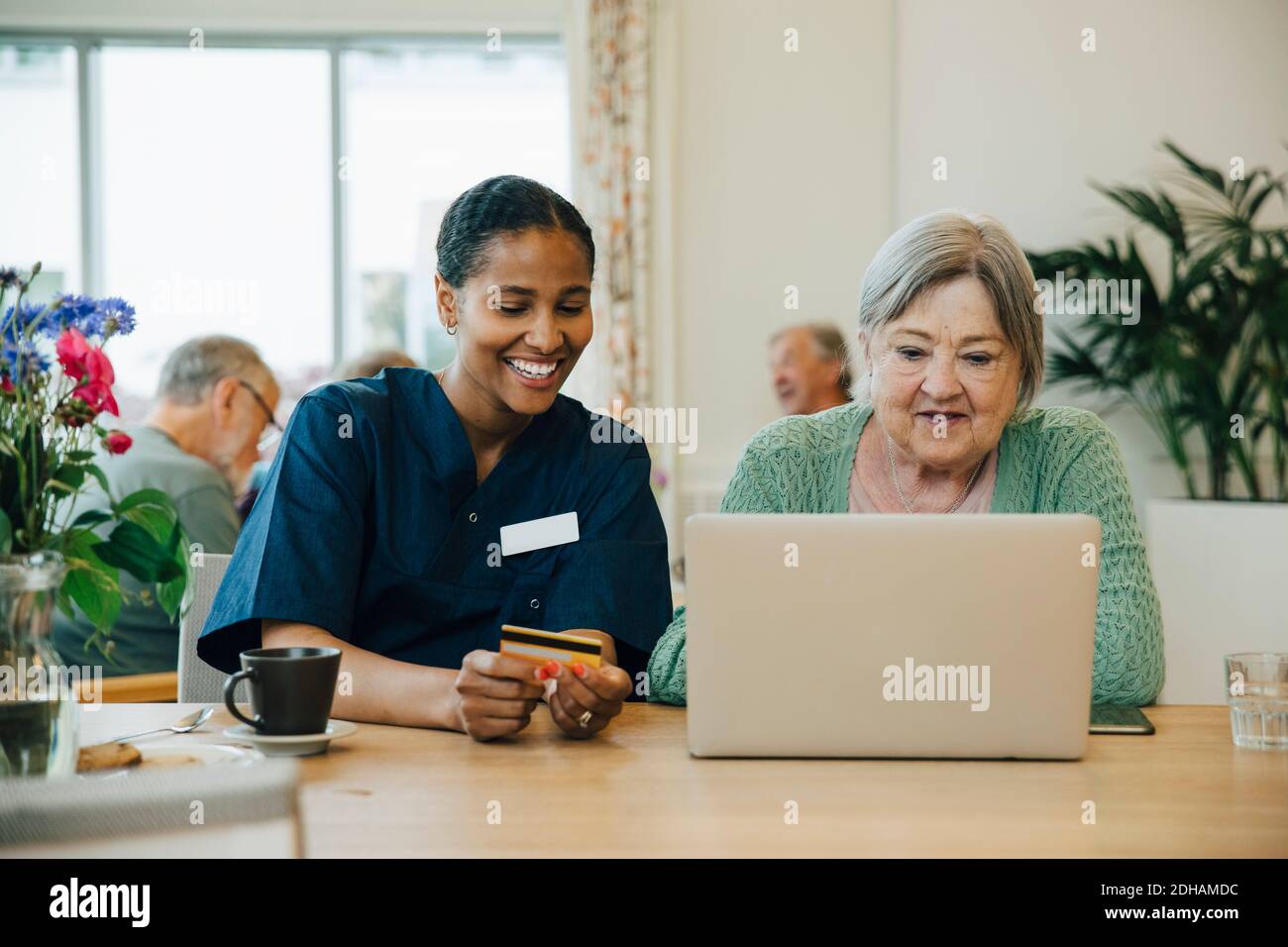 Lächelnd weibliche Betreuer Unterstützung ältere Frau tun Online-Shopping mit Kreditkarte und Laptop im Pflegeheim Stockfoto