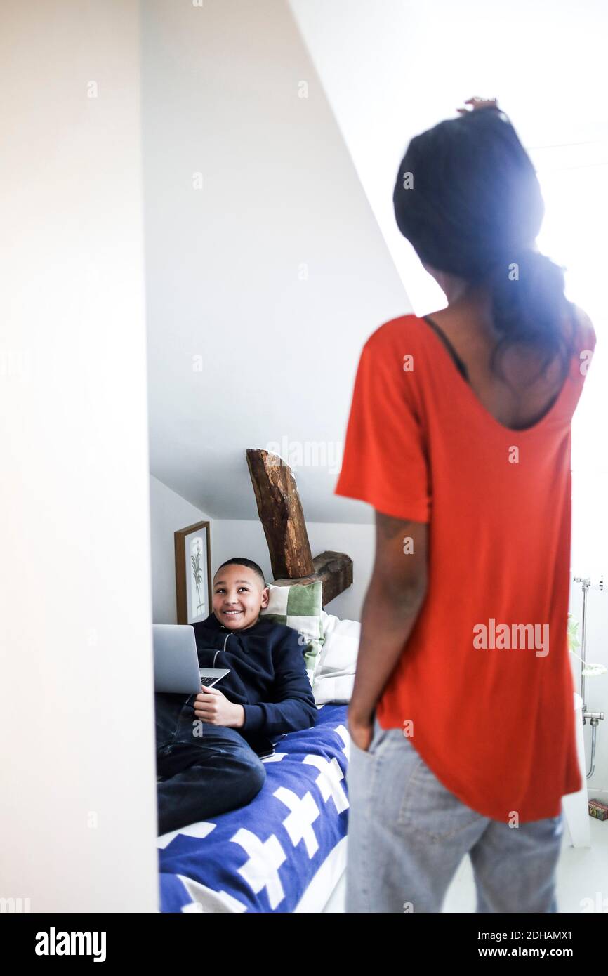 Mutter schaut auf glücklichen Jungen mit Laptop im Bett liegen Zu Hause Stockfoto