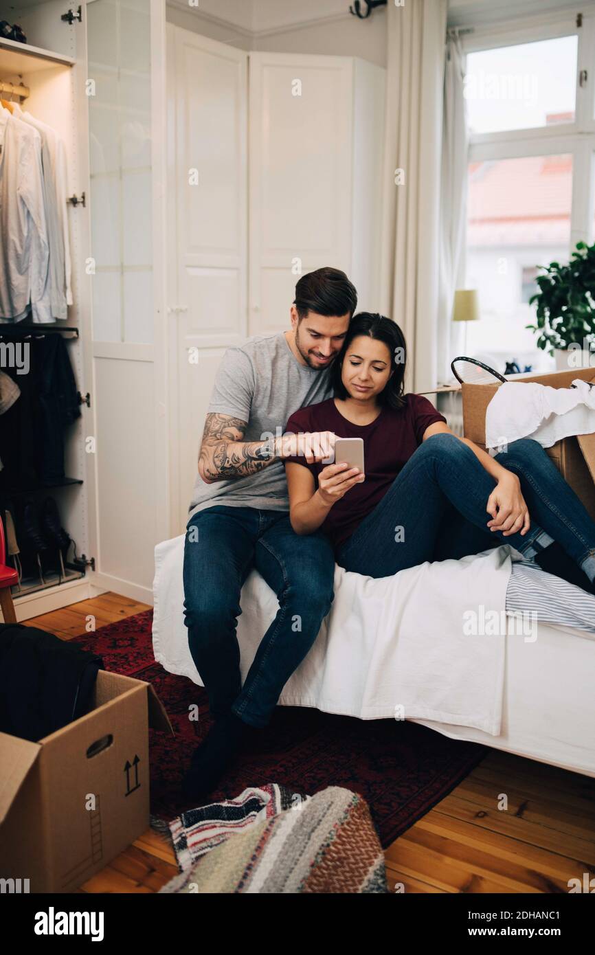 Paar mit Handy, während auf dem Bett im Schlafzimmer ruhen Stockfoto